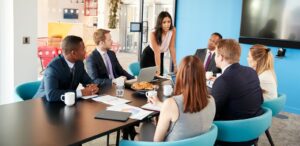 Female manager stands addressing colleagues in meeting room